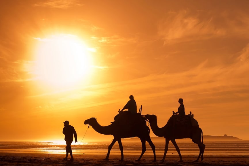 Couple riding camels along the beach in Essaouira, Morocco