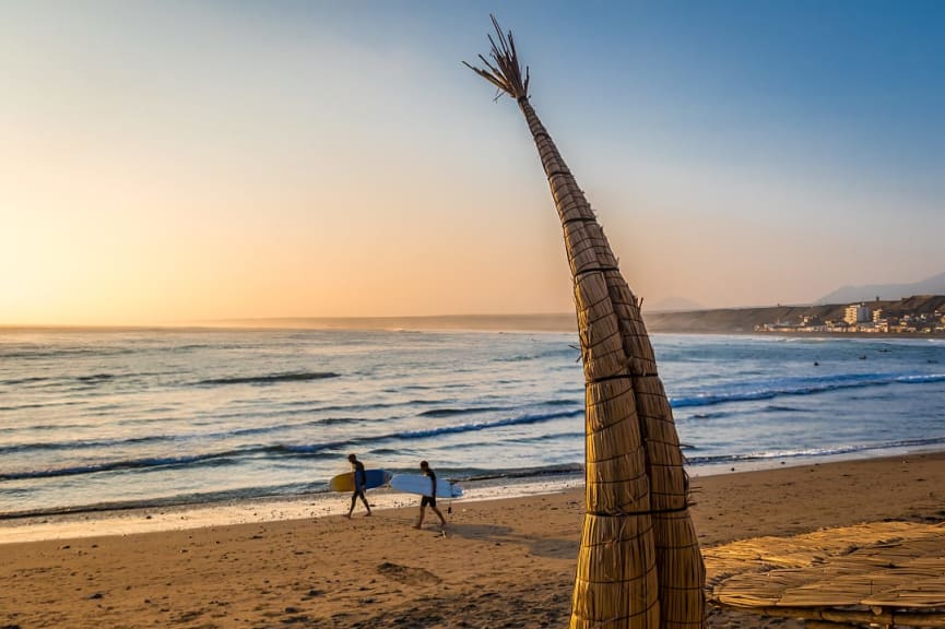 Surfers at Huanchaco Beach and the traditional reed boats in Peru