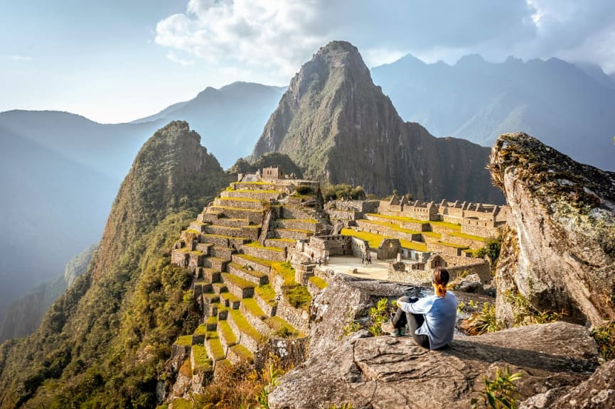 Woman sitting on a rock admiring the ruins of Machu Picchu in Peru