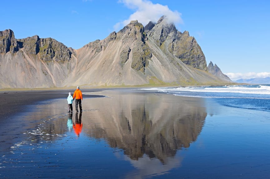 Father and son, walking on black sand at Stokksnes beach, enjoying scenery of Vestrahorn mountains in Iceland