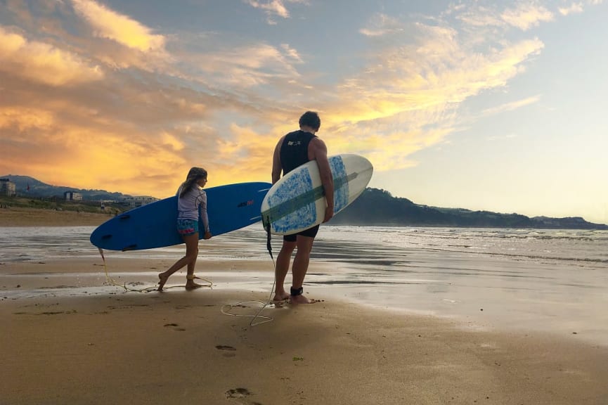 Father and daughter walking with surfboards on the beach in Spain