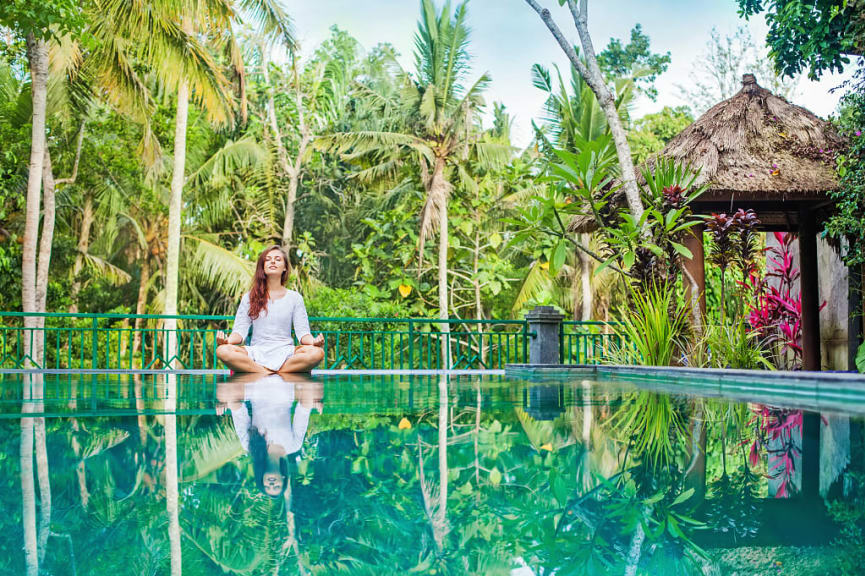 Woman meditating poolside at luxury resort in Bal