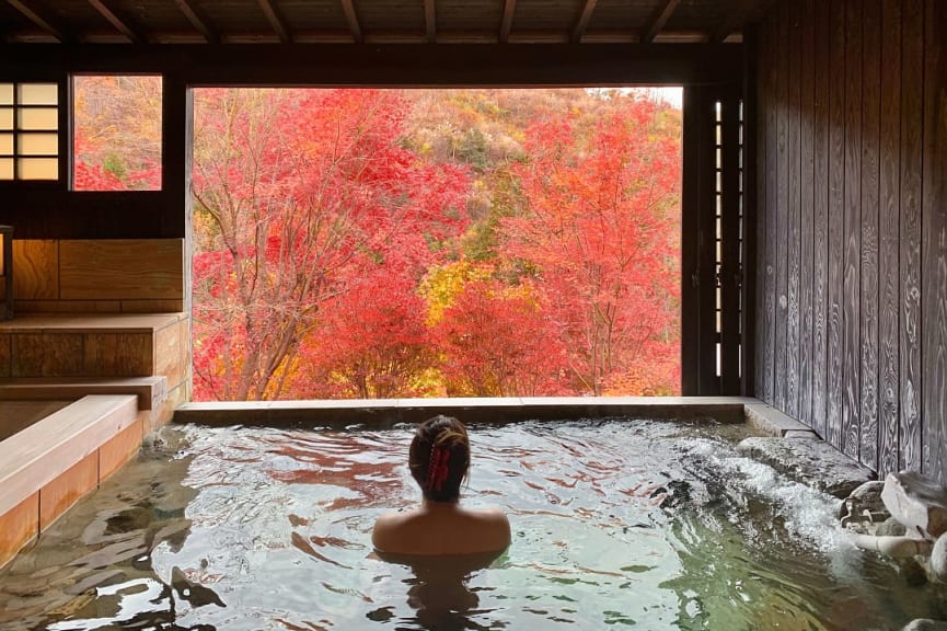 Woman soaking in an onsen while looking at the fall foliage