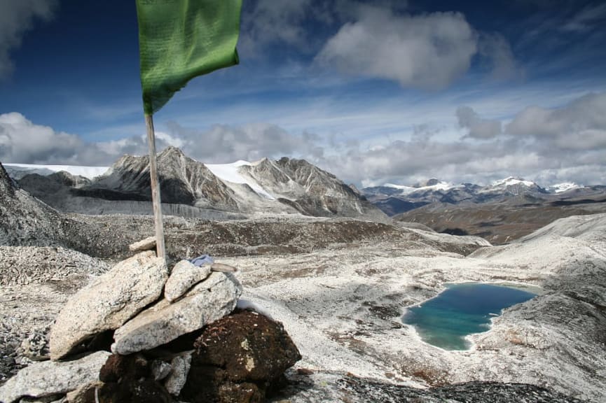 Flag posted in rocks flying from viewpoint at Rinchen Zoe La pass in Bhutan with scenic peaks, rocky valley with alpine lake