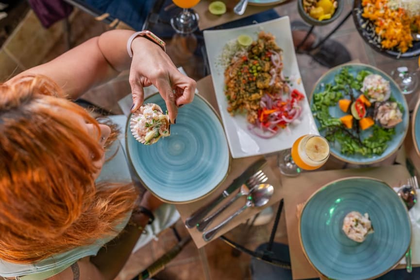 Overhead view of woman eating at a table filled with Peruvian food