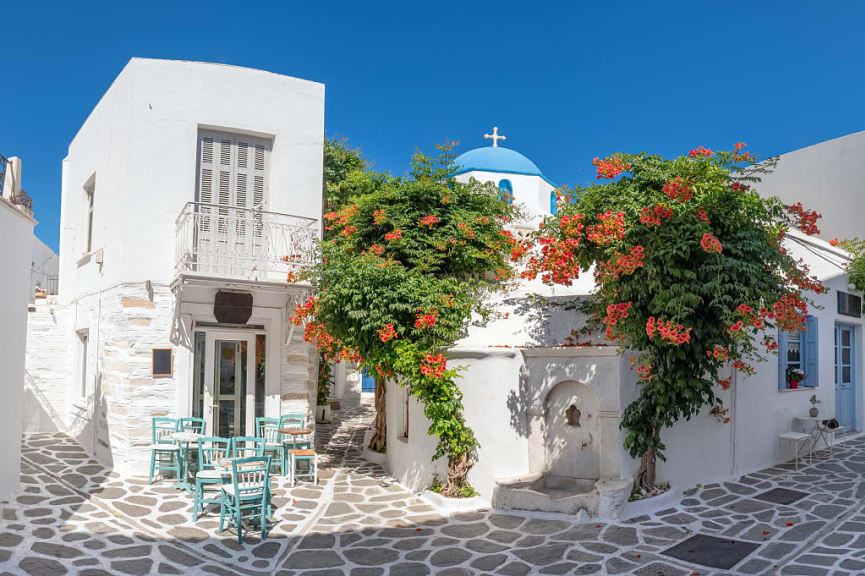 Narrow street with cozy outdoor cafe and traditional Greek church in Parikia town on Paros island, Cyclades.
