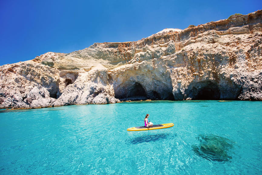 Teenager girl enjoying turquoise waters of the Aegean sea from a paddleboard during summer vacation in Milos, Greece