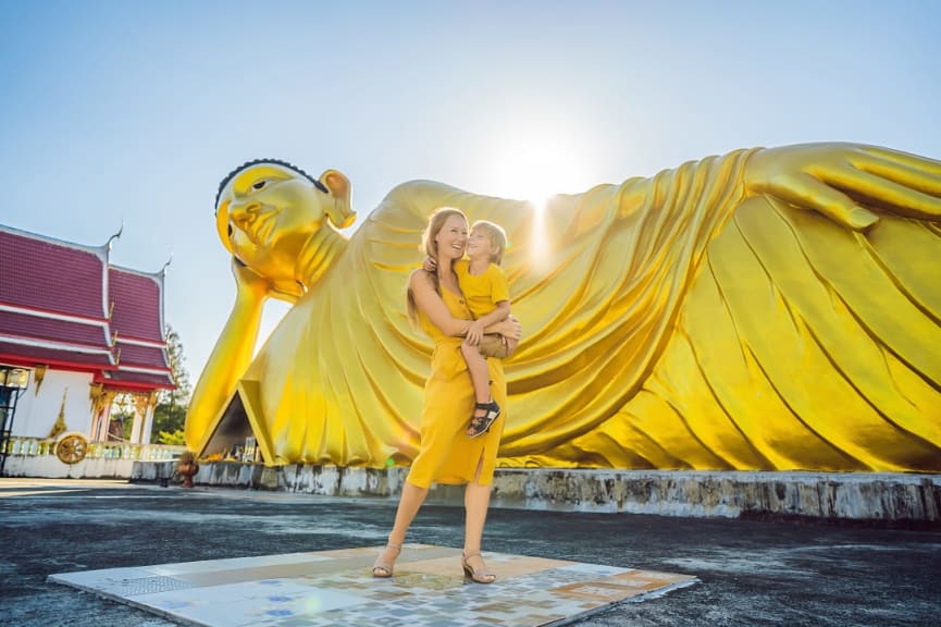 Mother and son travelers standing in front of lying buddha statue in thailand