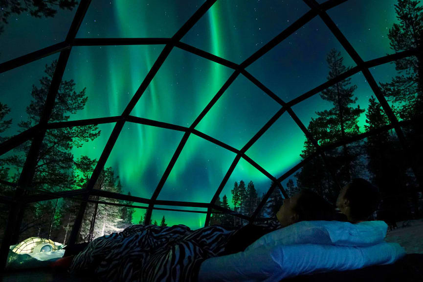 Couple watching the northern lights from inside a glass igloo in Finland