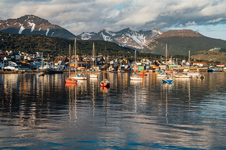 Colorful boats in the harbor of Ushuaia, Argentina, with snow-capped mountains and town in the background