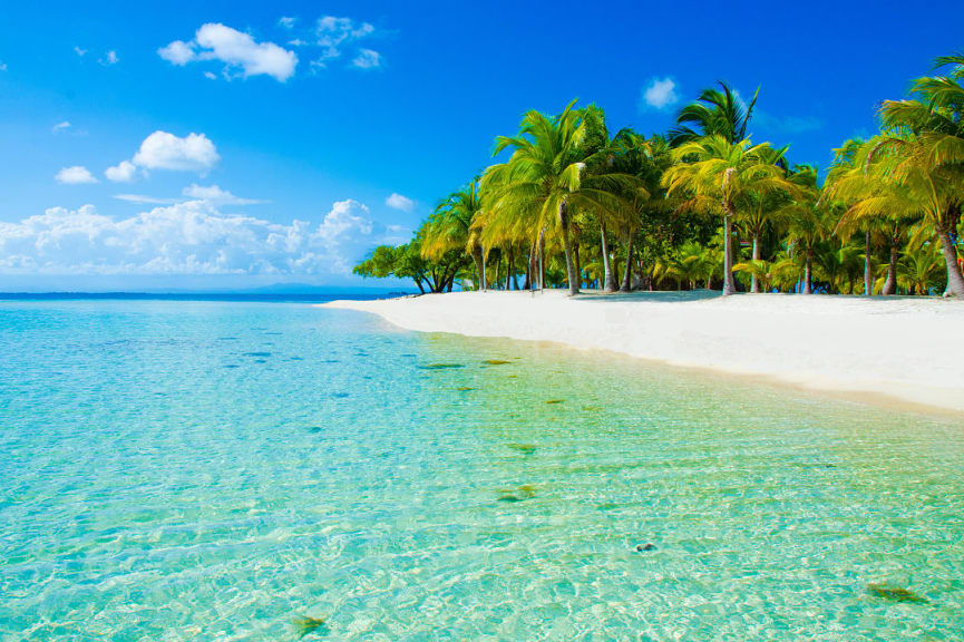 Crystal clear water, white sands and palm trees in South Water Caye, Belize