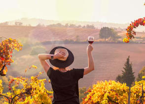 Woman raising a glass of wine, enjoying the view at sunset in Tuscany