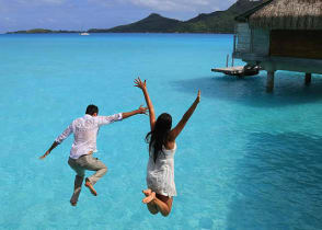 Happy young couple jump into the water from their over water bungalow in Bora Bora