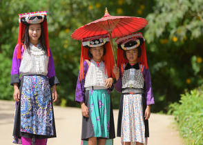 Three young Lahu Tribe girls in custom dress, smiling among the sunlight in Thailand.