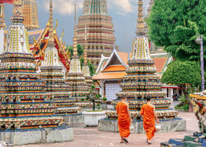 Two monks in colorful orange robes walking through Wat Pho Temple in Bangkok, Thailand