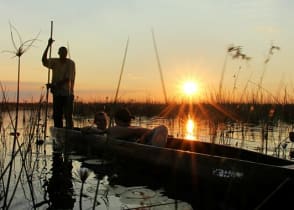 Couple on mokoro boat safari at sunset in the Okavango Delta, Botswana