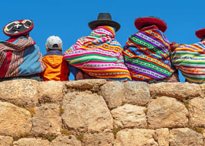 Native Peruvian women pose on a rock wall with a young tourist in Cusco