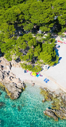 Emerald water laps against rocky cove and sun-dappled beach.