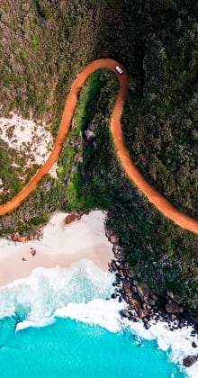 Winding dirt road leads to turquoise ocean and sandy beach.