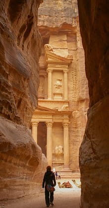 Traveler approaches Petra’s iconic carved facade through narrow canyon.