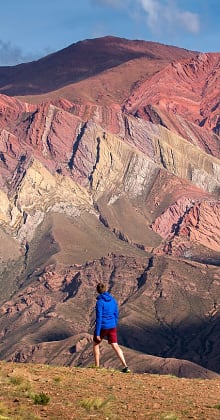 Hiker approaches colorful striped mountains under clear blue sky.