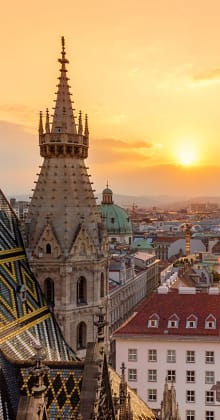Cathedral spire and tiled roof at sunset over Vienna skyline.