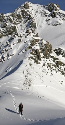 Solo hiker ascending snow-covered ridge toward dramatic alpine mountain peak.
