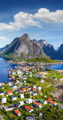 Colorful coastal village below towering fjord mountains in northern Norway.