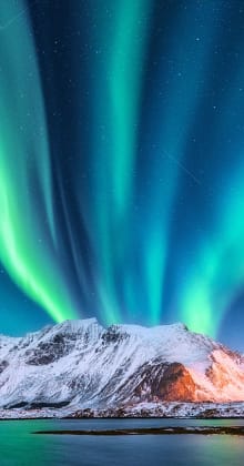 Northern Lights dance above snowy mountains and icy coastal landscape.