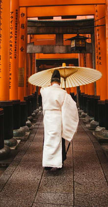 Person in traditional attire walks under torii gates with umbrella.