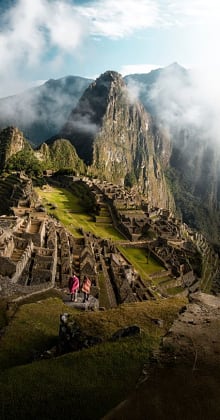 Couple overlooking Machu Picchu ruins with misty Andes mountain backdrop.