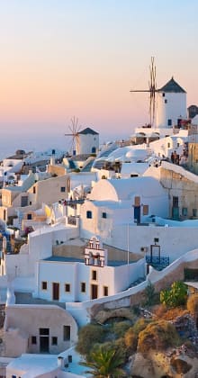Whitewashed buildings and windmills on a cliffside at sunset.