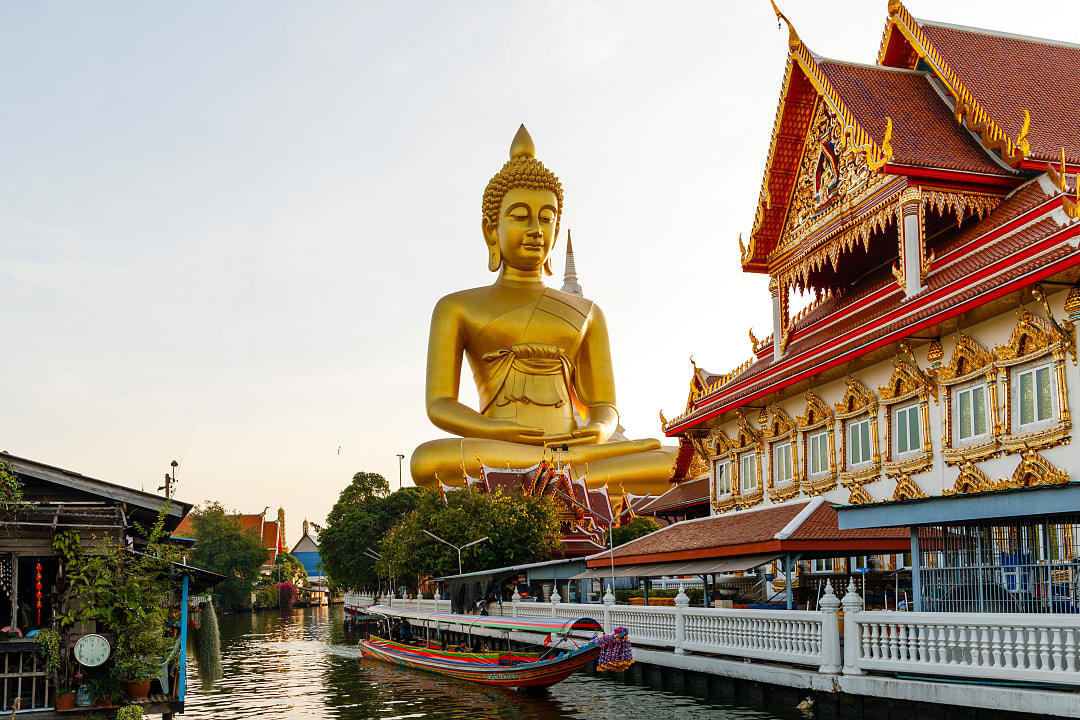 Golden Buddha statue and temple beside canal in Bangkok, Thailand.
