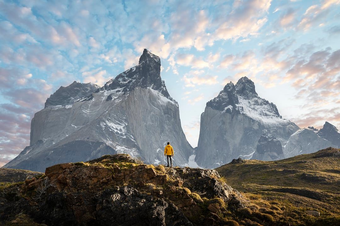 Lone hiker in a yellow jacket standing before the dramatic peaks of Torres del Paine in Patagonia at sunrise.