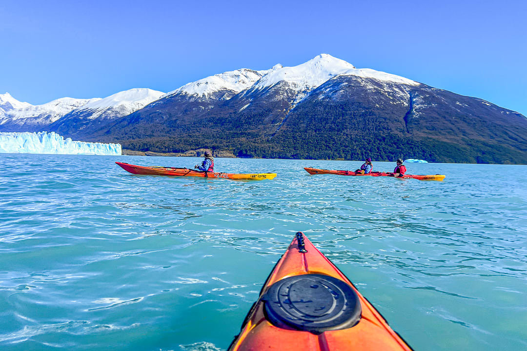 Kayakers paddle near icebergs on a pristine lake surrounded by snowy mountains in Patagonia, South America.