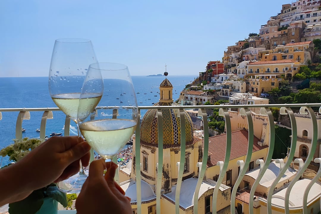 Couple holding wine glasses with Positano view on the Amalfi Coast