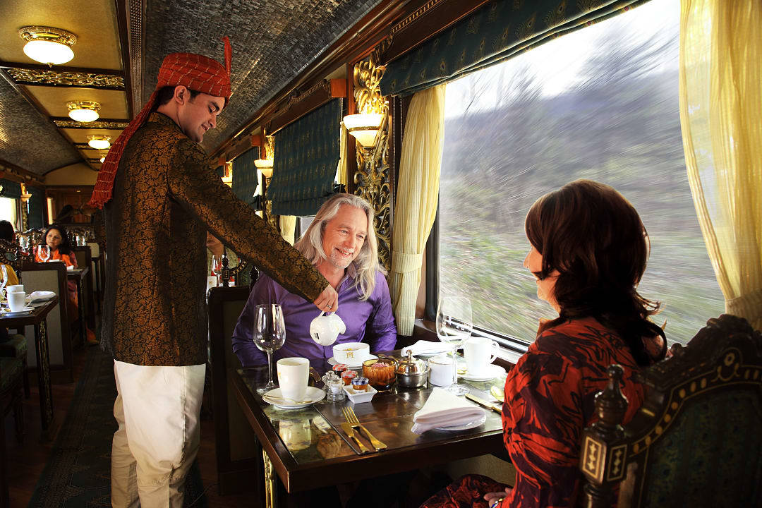 Elegant train dining with waiter serving tea to smiling guests.