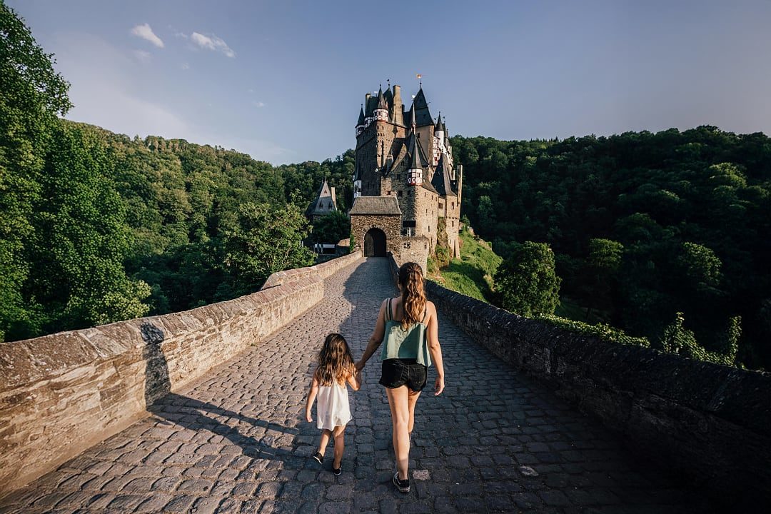 Burg Eltz in Germany with a mother and daughter walking on a cobblestone bridge surrounded by forest