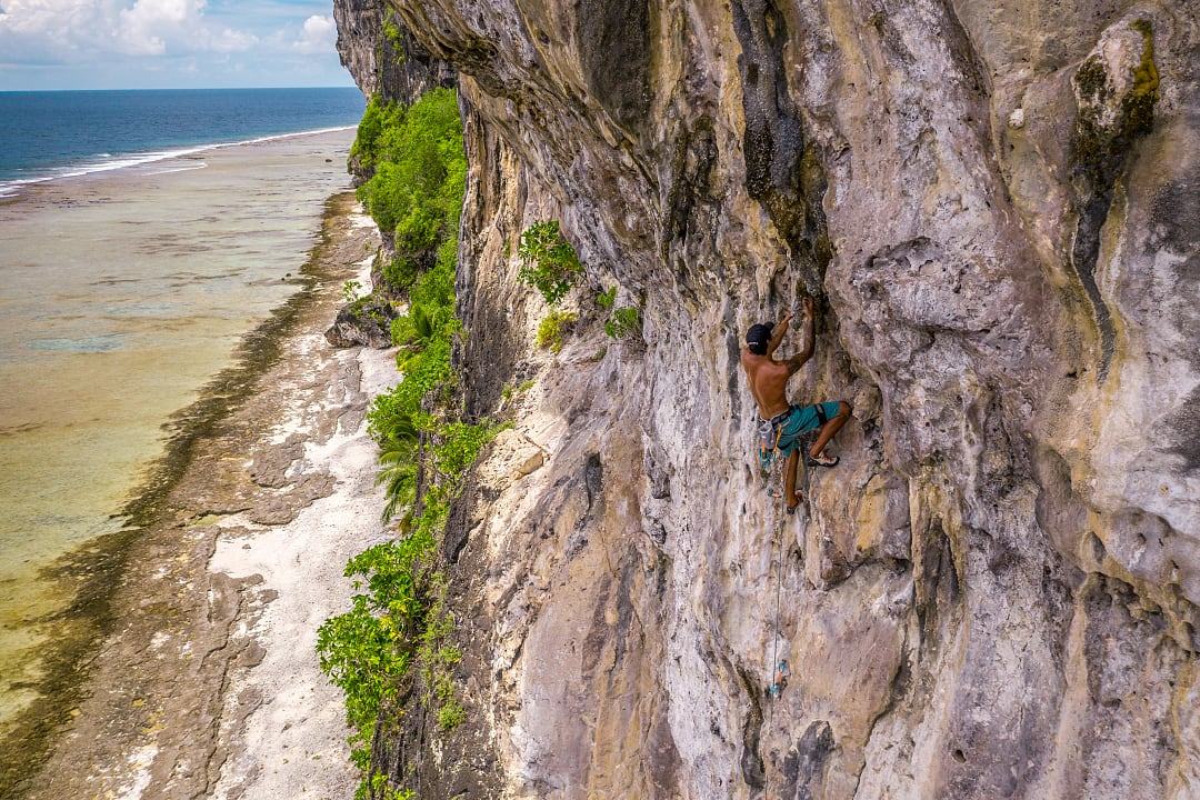 Rock climber scaling limestone cliffs above the beach in Makatea, French Polynesia, with ocean views