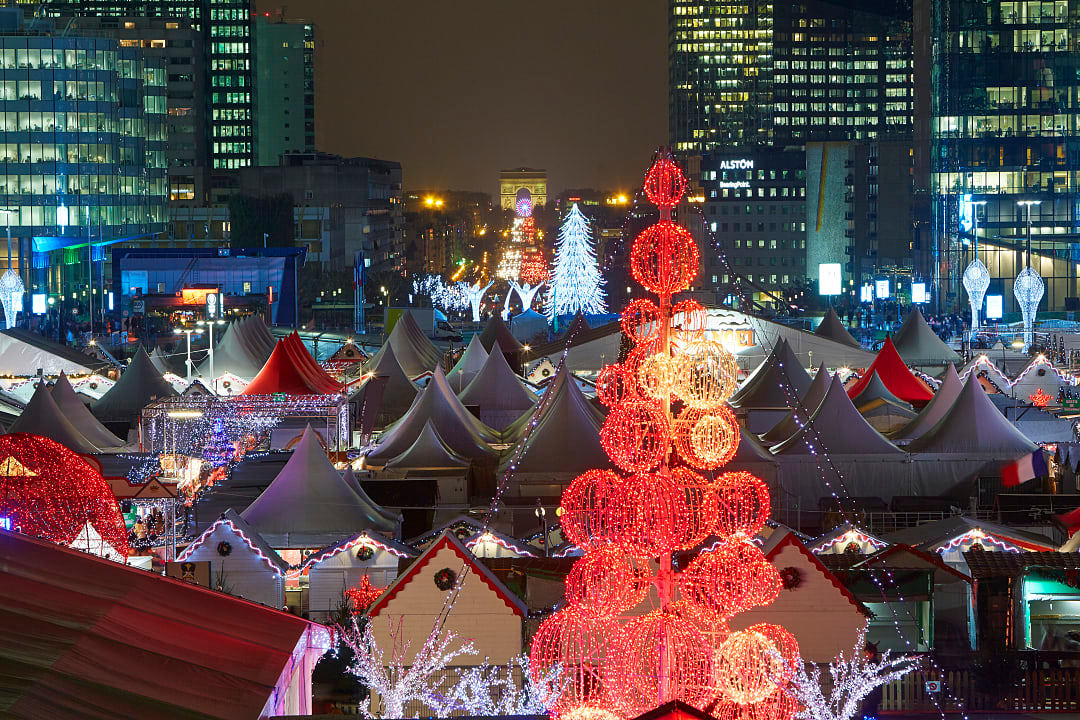 Festive La Défense Christmas Market in Paris, France with illuminated red spheres and white tents and Arc de Triomphe visible in background