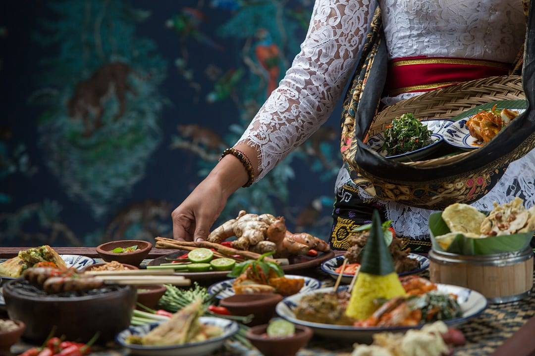 Woman serving food traditional to Bali, such as nasi tumpeng,satay skewers, fresh herbs, vegetables, and vibrant spices.