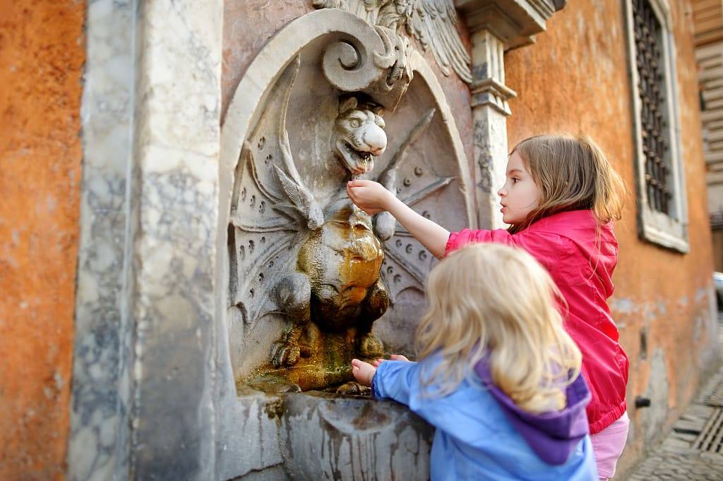 Two sisters having fun at a small water fountain in Rome
