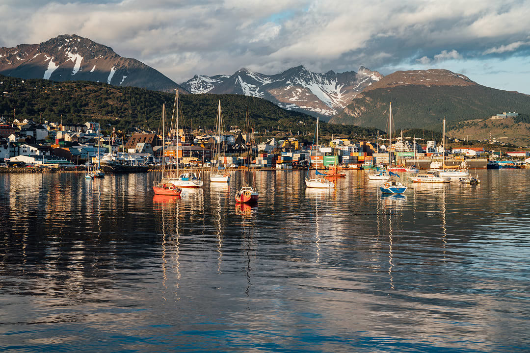 Colorful boats in the harbor of Ushuaia, Argentina, with snow-capped mountains and town in the background