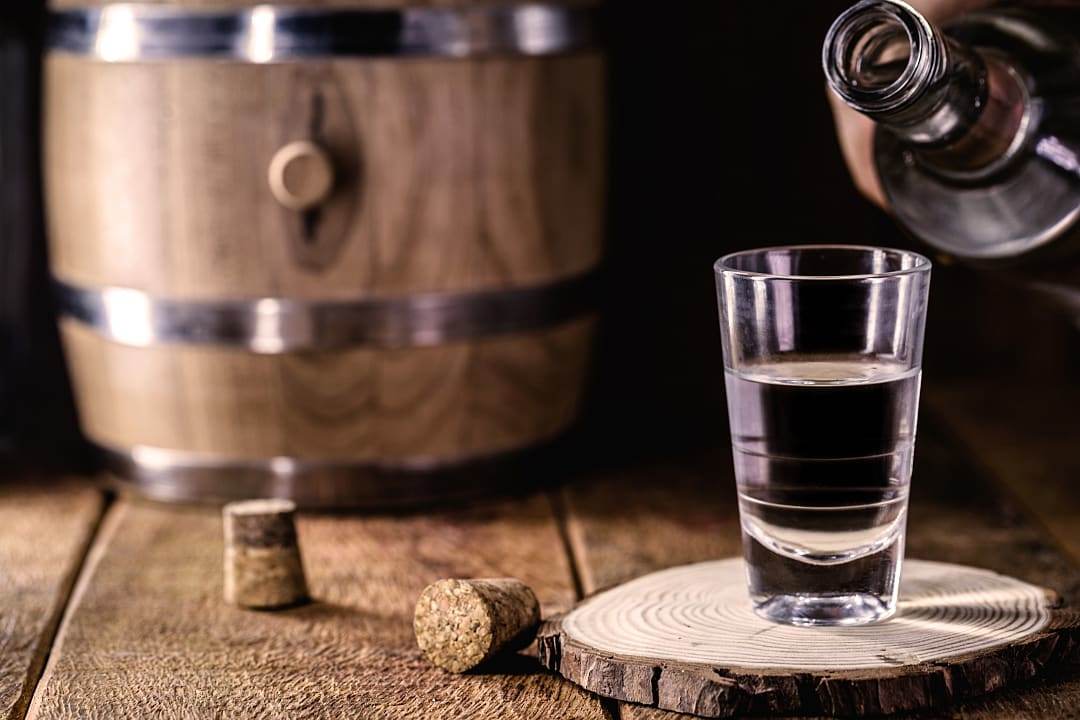 Spirit being poured in a shot glass, in a distillery.