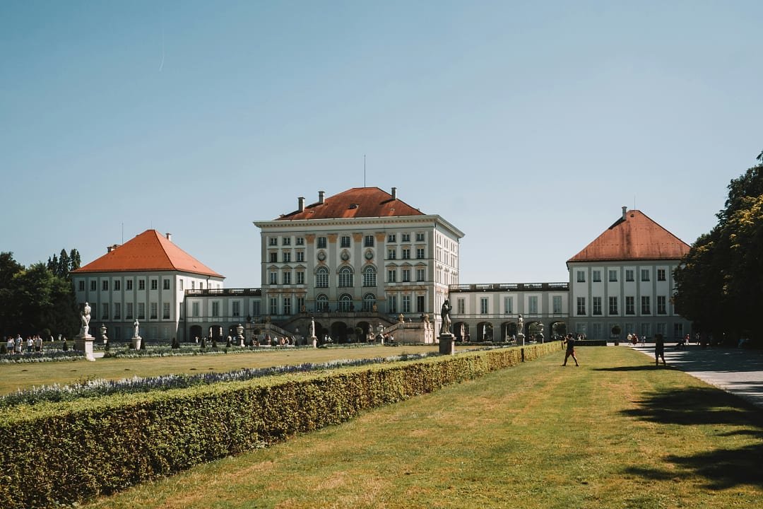 Nymphenburg Palace in Munich, Germany, with manicured gardens and visitors enjoying a sunny day.