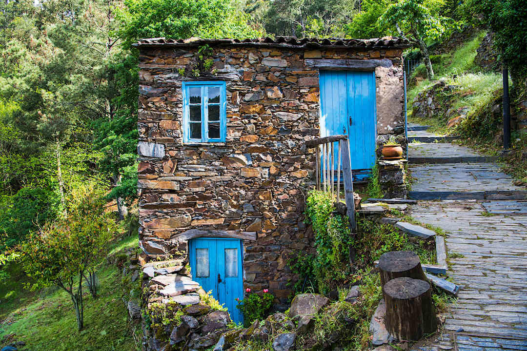 Rustic schist house with bright blue doors along a stone path in Portugal