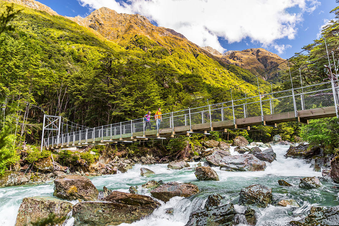 Hiking couple crossing river bridge along the Routeburn Track in New Zealand