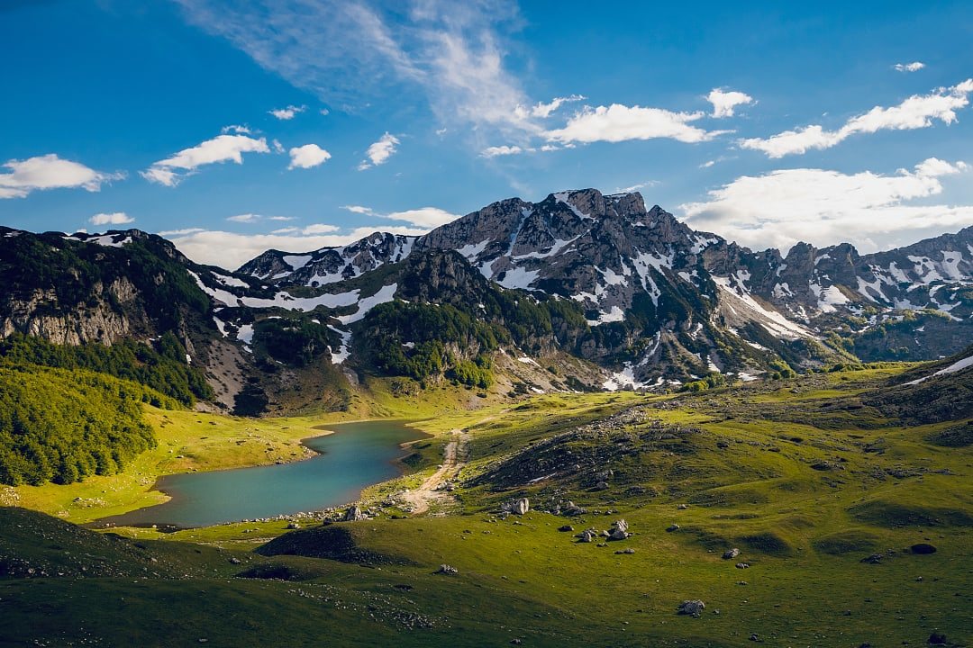 Small blue glacial lake nestled between green hills and mountains.