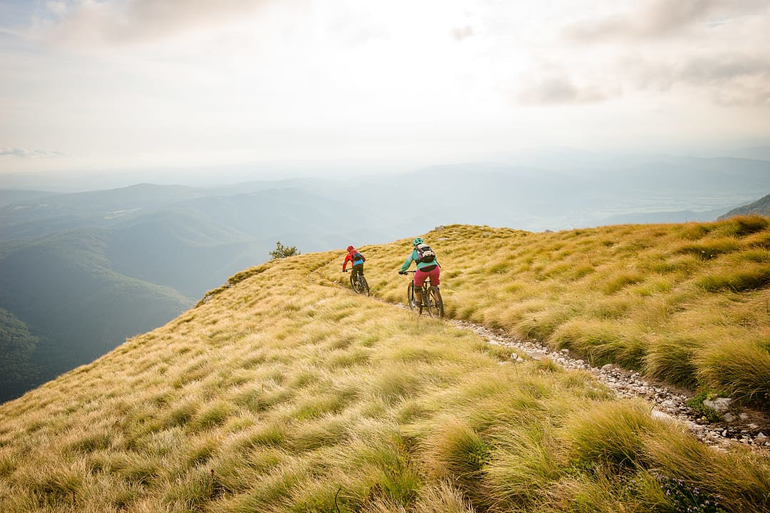 Two mountain bikers riding on grassy mountain ridge