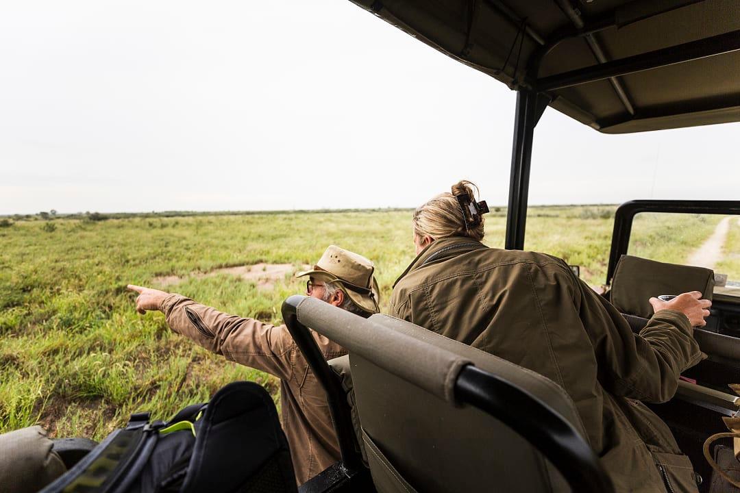 Two people in a safari vehicle look out at the vast green landscape of a private conservancy at dusk.